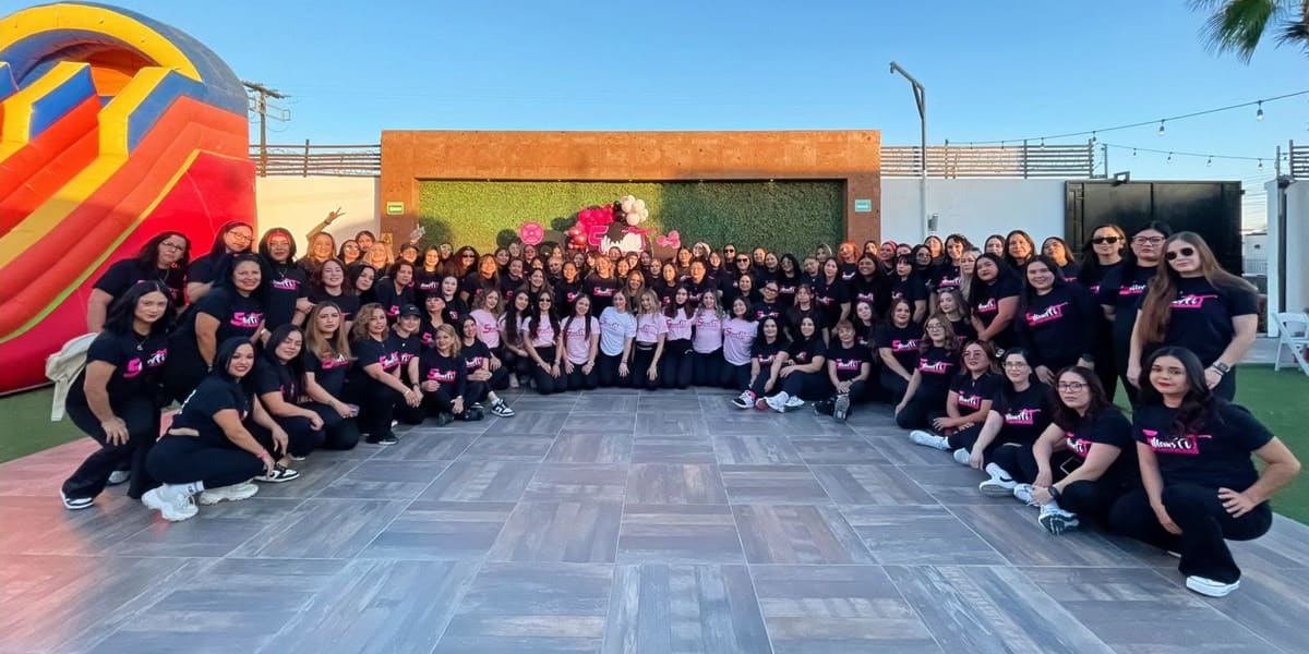 Una multitud de alumnas con la playera de los 5 años de Moms Fit, reunidas en un jardín al atardecer
