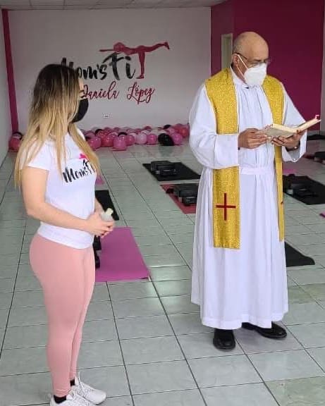 Un sacerdote bendice el salón de Moms Fit, con los tapetes listos y globos rosas al fondo
